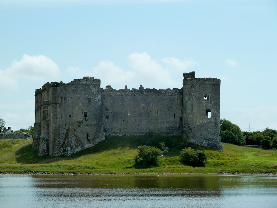 A medieval castle with a moat, surrounded by greenery and a clear sky.