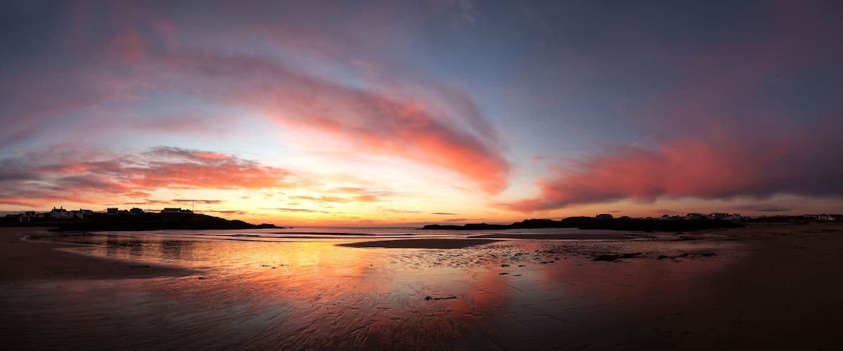 A sunset over a beach with a dramatic sky and calm waters reflecting the colors.