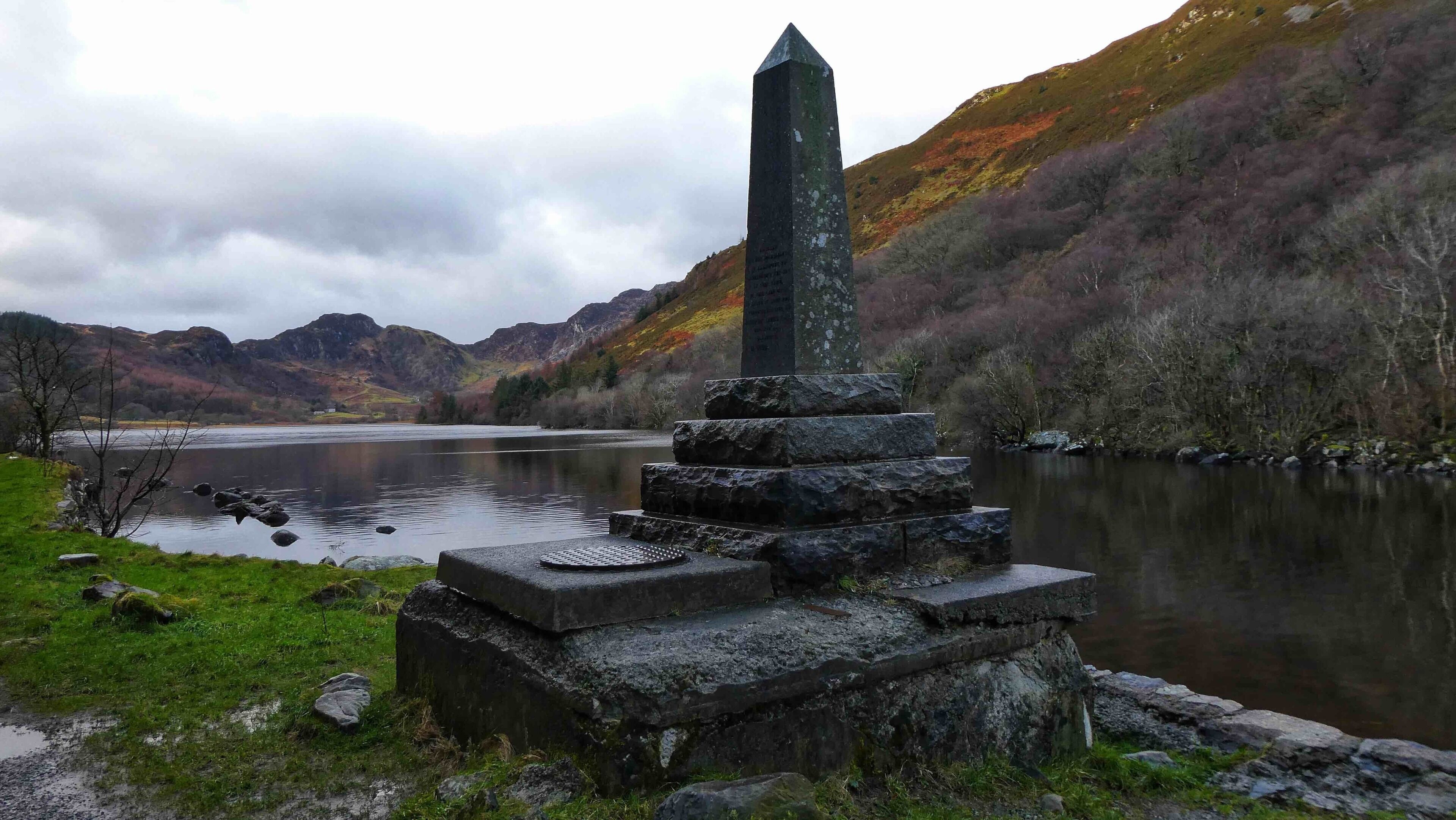 A stone monument by a lake with mountains in the background.