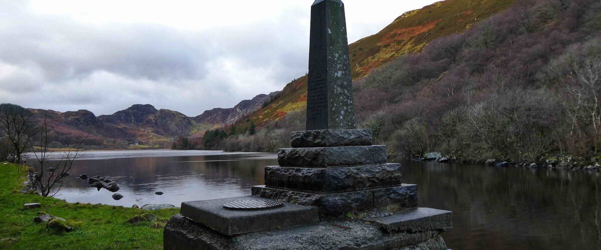 A stone monument by a lake with mountains in the background.