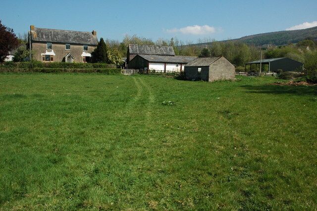 A rural landscape with a large grassy field, a farmhouse, and a barn.