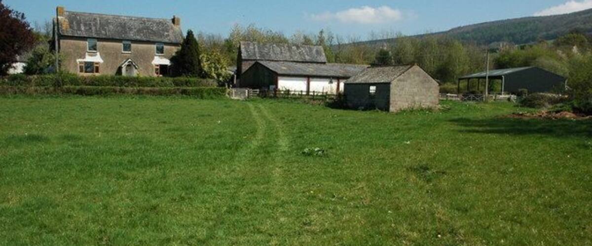 A rural landscape with a large grassy field, a farmhouse, and a barn.