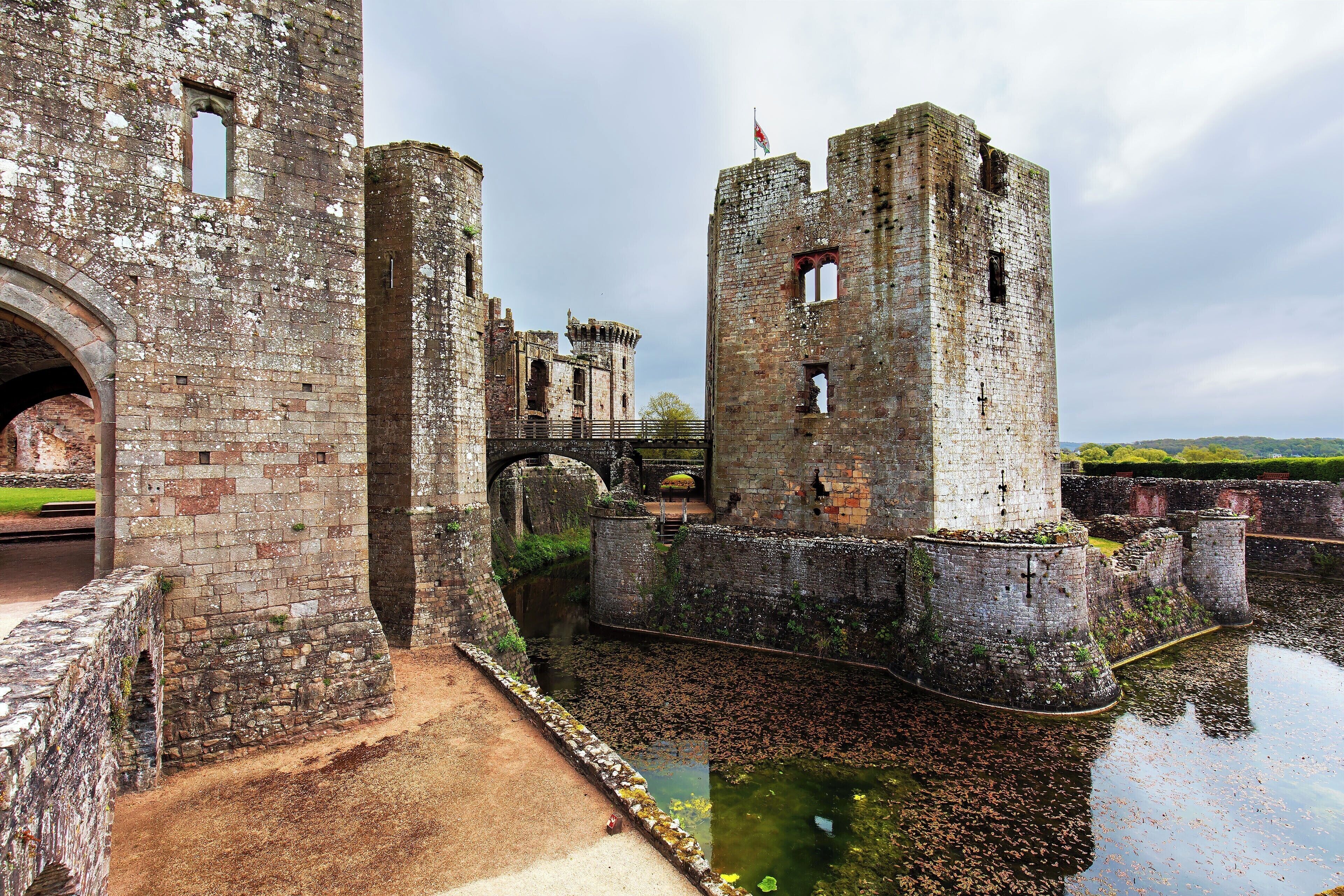 A historic castle with a moat, stone walls, and a flag on top of one tower.