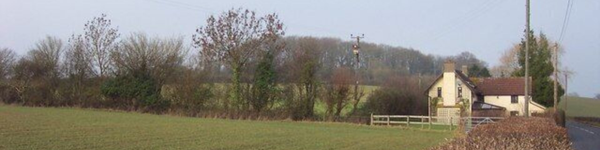A rural landscape with a field, a small house, and a fence.