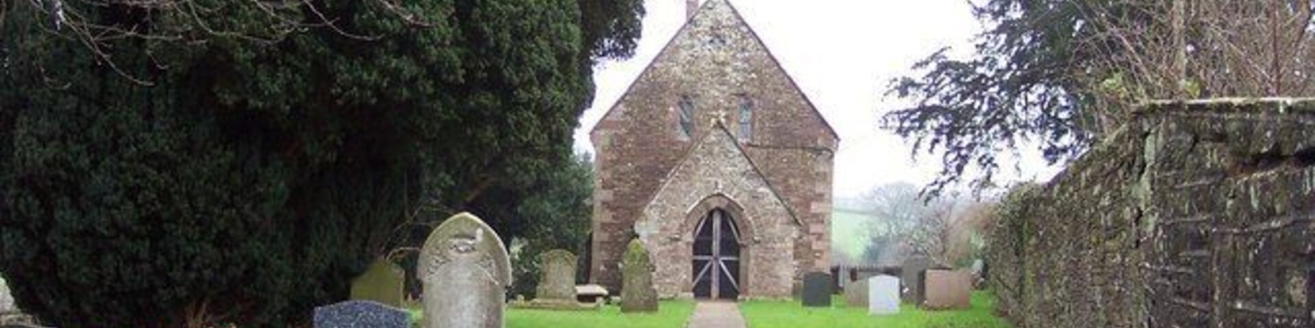 A church with a pointed steeple, surrounded by a cemetery with headstones and a pathway leading to the entrance.