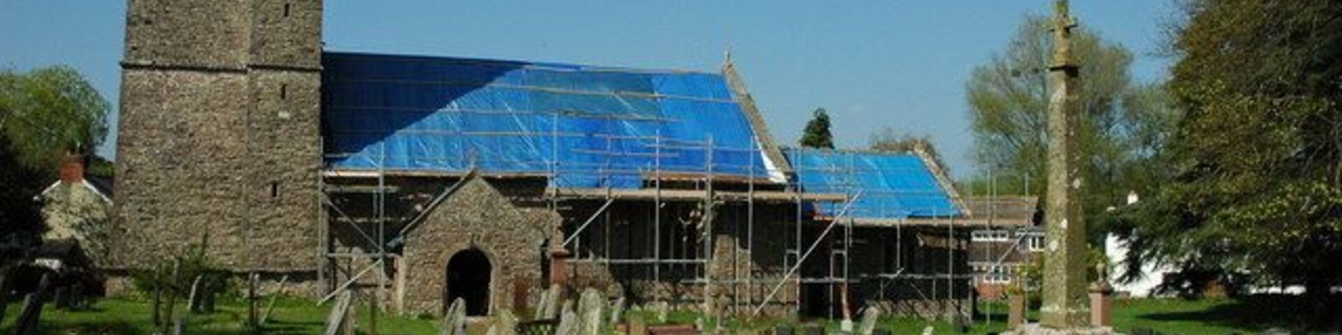 A church with a stone tower and a blue roof under construction.