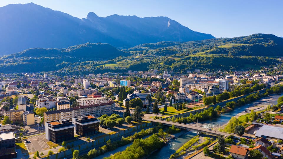 A cityscape with a river, buildings, and mountains in the background.
