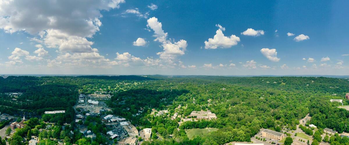 A panoramic view of a town surrounded by dense forests, with a highway curving through the landscape.