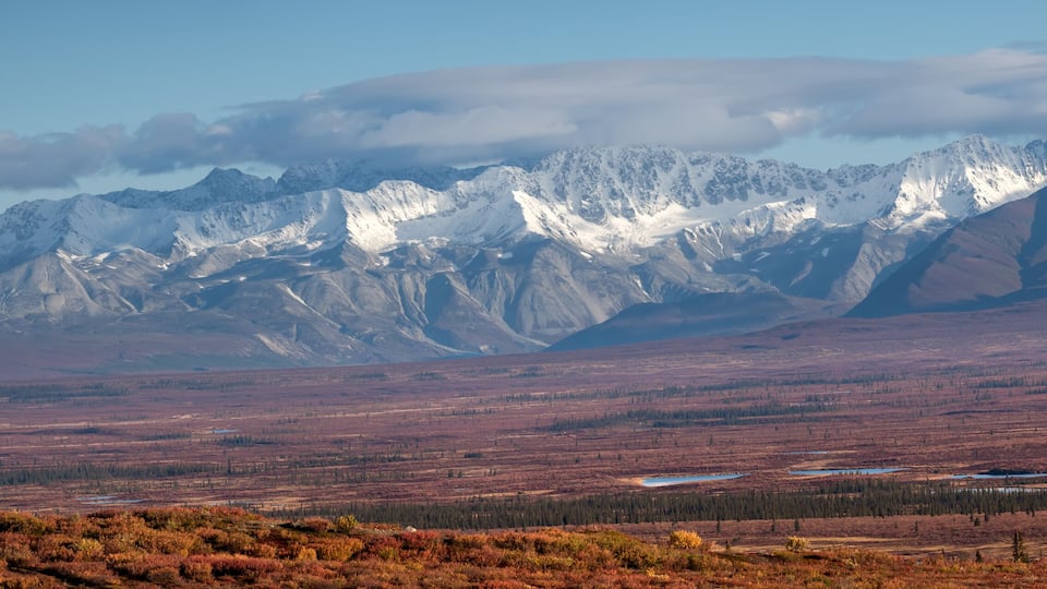 A mountainous landscape with snow-capped peaks and a flat, barren foreground.