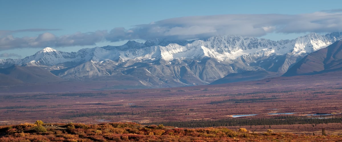 A mountainous landscape with snow-capped peaks and a flat, barren foreground.