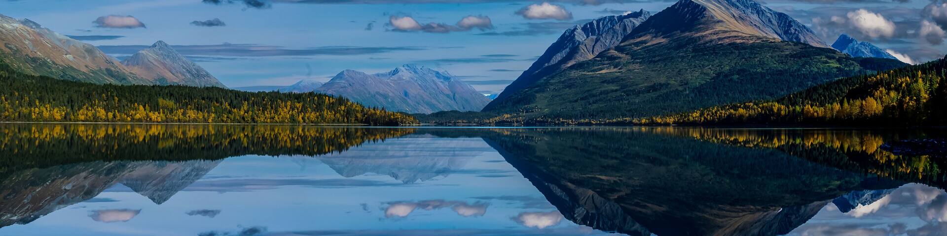 A tranquil lake reflecting mountains and a forested shoreline.