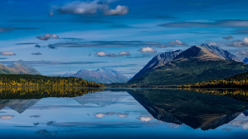 A tranquil lake reflecting mountains and a forested shoreline.