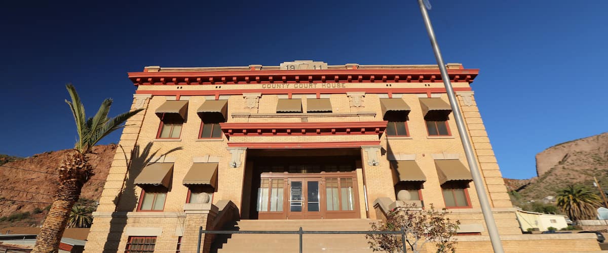 A courthouse with a red and beige facade, a flagpole with an American flag, and a palm tree in the foreground.