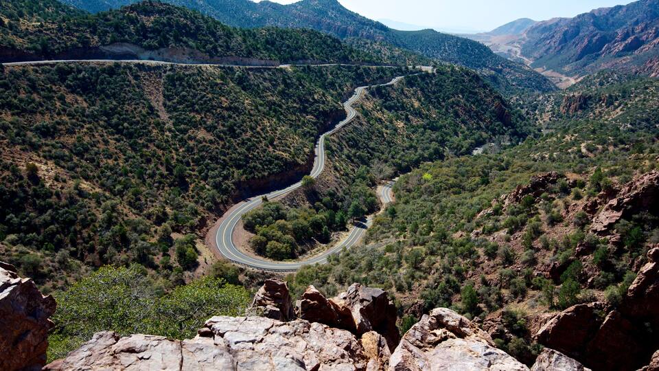 A winding mountain road through a canyon with rocky outcrops and dense vegetation.