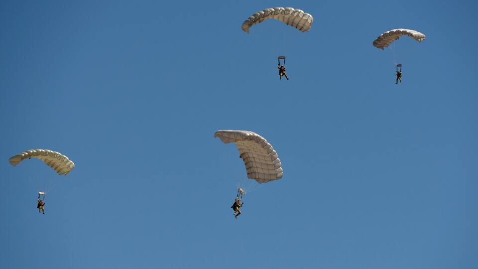 A clear blue sky with five parachutists descending.