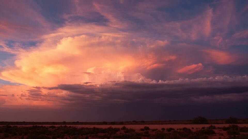 A desert landscape with sparse vegetation and a dramatic sunset sky.