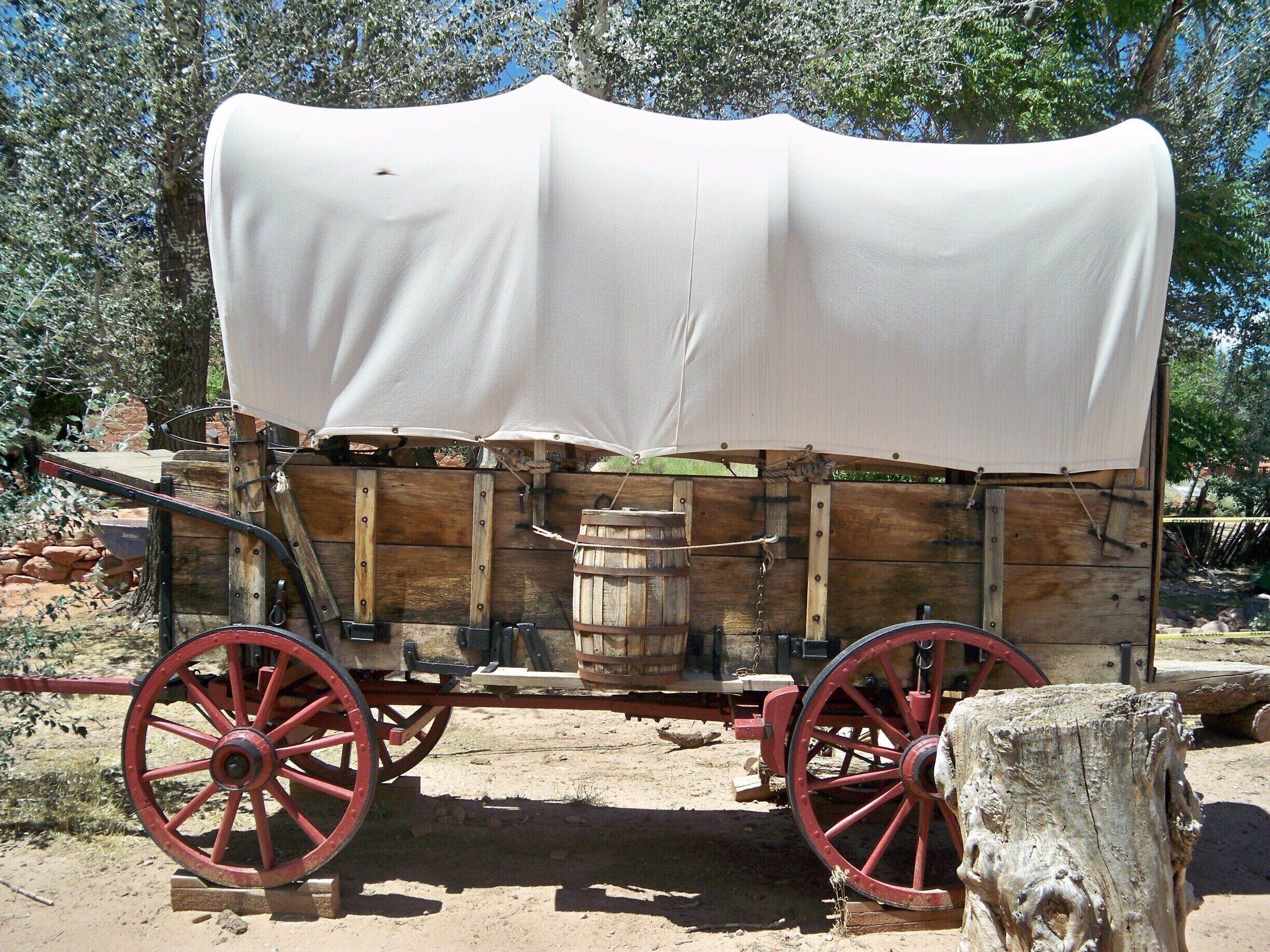 A covered wagon with red wheels and a white tarp, parked outdoors.