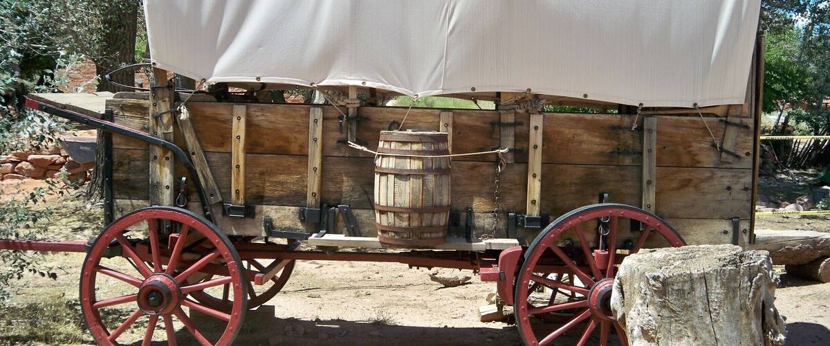 A covered wagon with red wheels and a white tarp, parked outdoors.