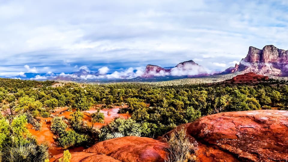 A mountainous landscape with red rock formations and dense green forests.