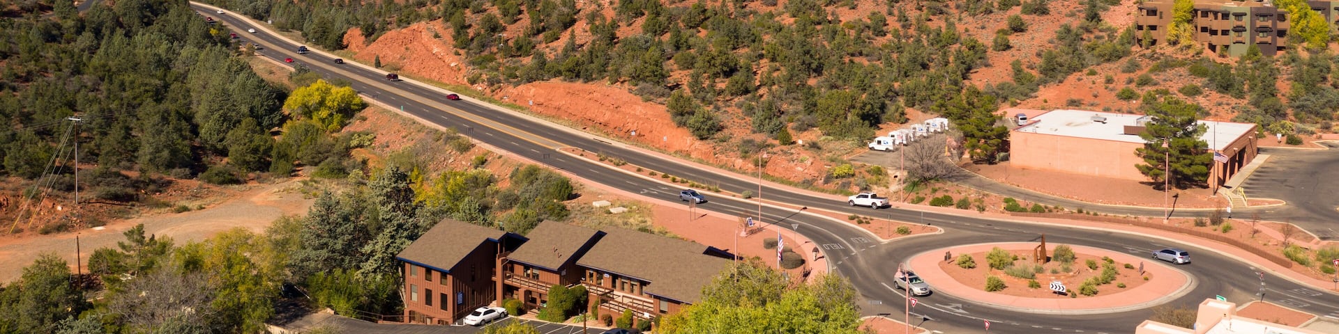 A highway curving through a desert landscape with red rock formations in the background.