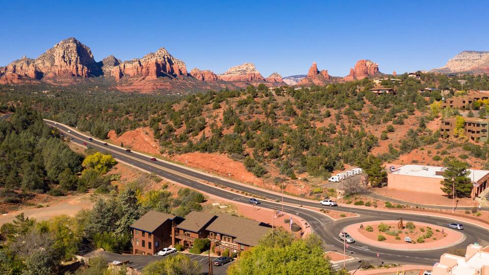 A highway curving through a desert landscape with red rock formations in the background.