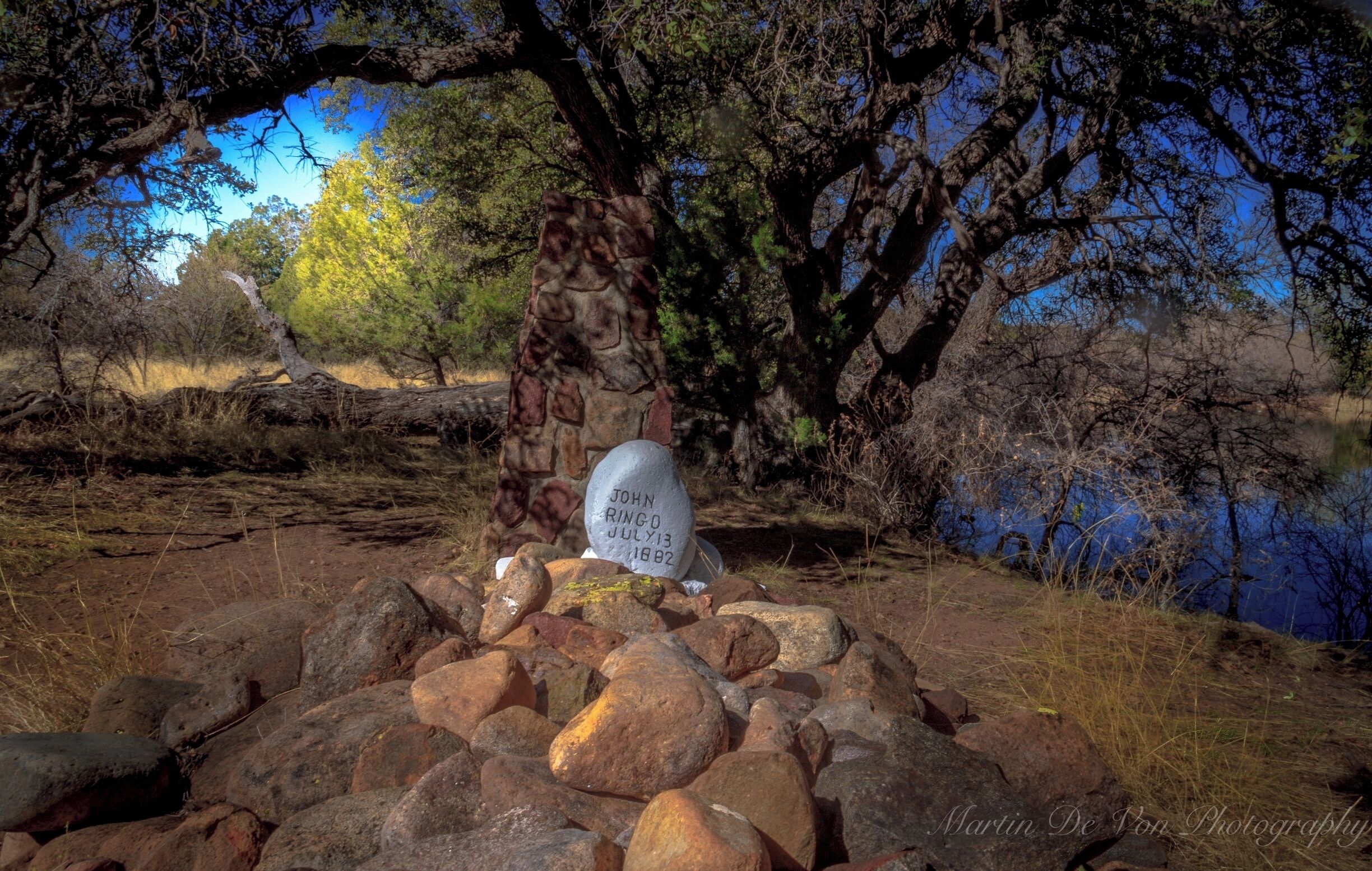 A gravestone with the inscription "John Ringo July 13, 1882" surrounded by rocks and trees.