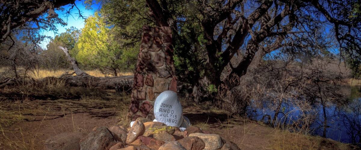 A gravestone with the inscription "John Ringo July 13, 1882" surrounded by rocks and trees.