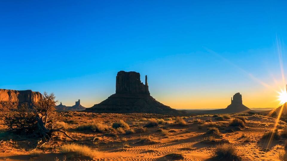 A desert landscape with rock formations and the sun setting in the background.
