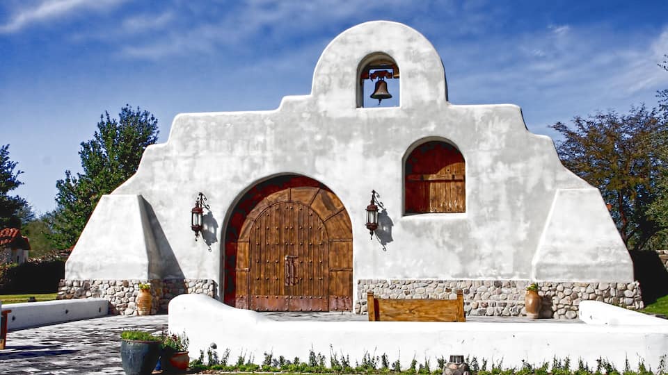 A white building with a bell tower, wooden doors, and stone accents.