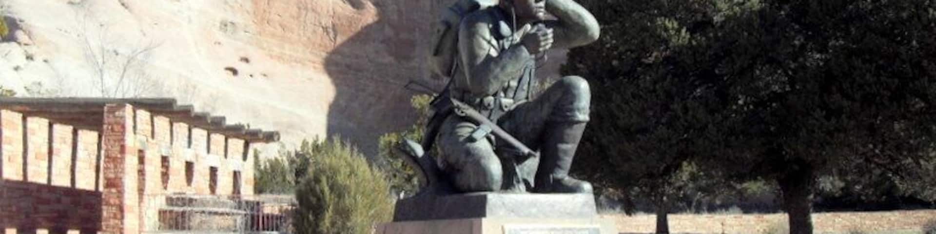 A statue of a soldier in a park with a mountainous backdrop.