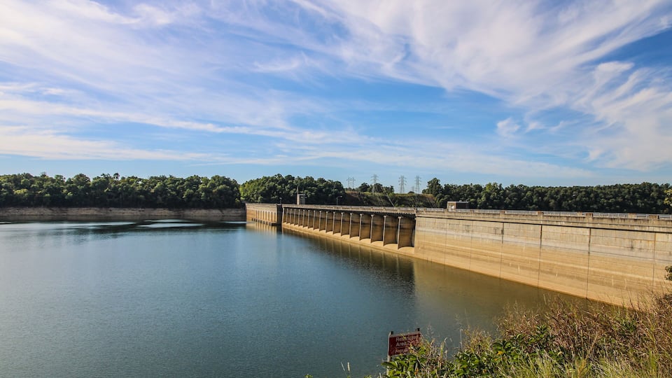 A dam with a reservoir, surrounded by trees and a clear sky.