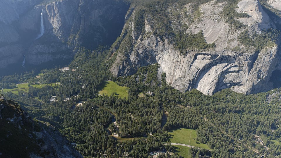 A mountainous landscape with a waterfall, dense forests, and a winding road.