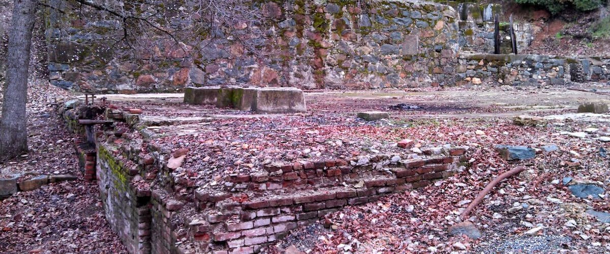 An ancient stone wall with brick foundations, surrounded by fallen leaves and scattered stones.