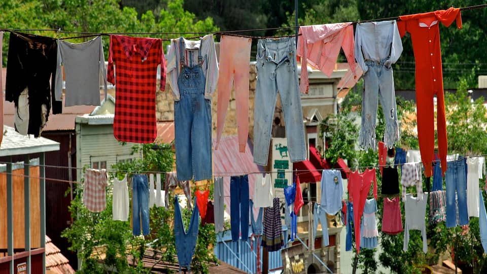 A clothesline with various garments hanging in a residential area with houses and greenery in the background.