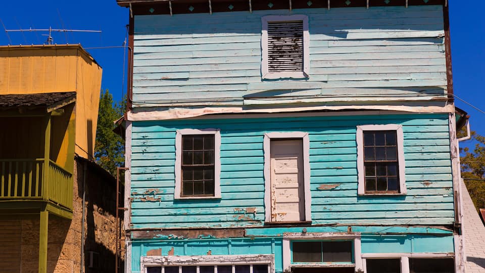 A two-story building with a blue exterior and white trim, featuring multiple windows and a visible chimney.