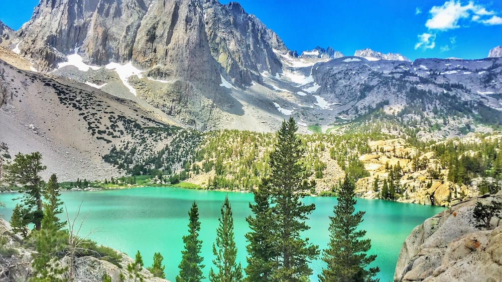 A mountain range with a turquoise lake and coniferous trees.