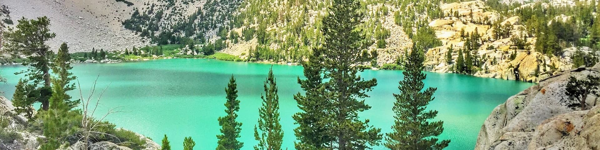 A mountain range with a turquoise lake and coniferous trees.
