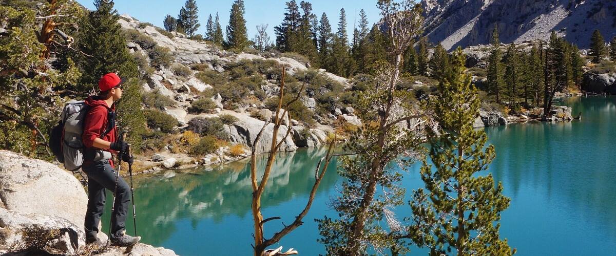A hiker on a rocky outcrop overlooking a turquoise lake surrounded by trees and mountains.