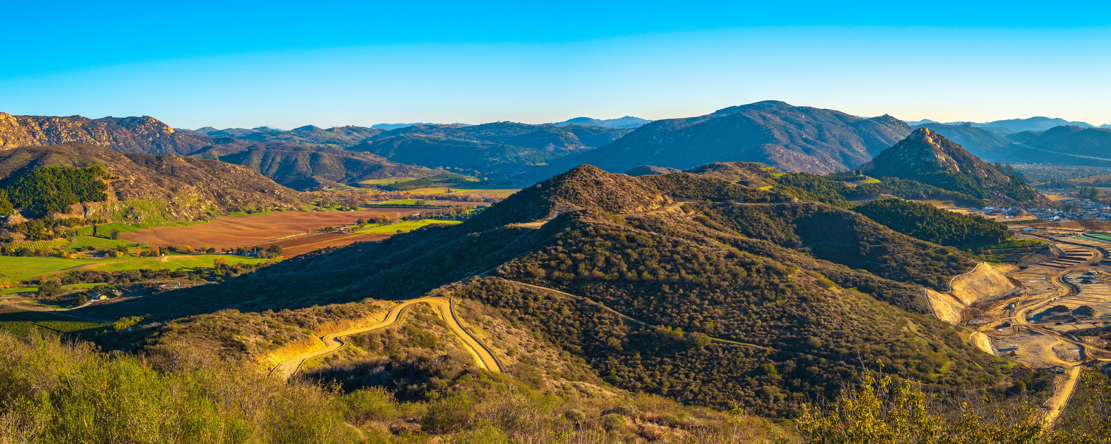 A mountainous landscape with winding roads, fields, and distant buildings.