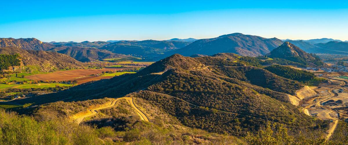 A mountainous landscape with winding roads, fields, and distant buildings.