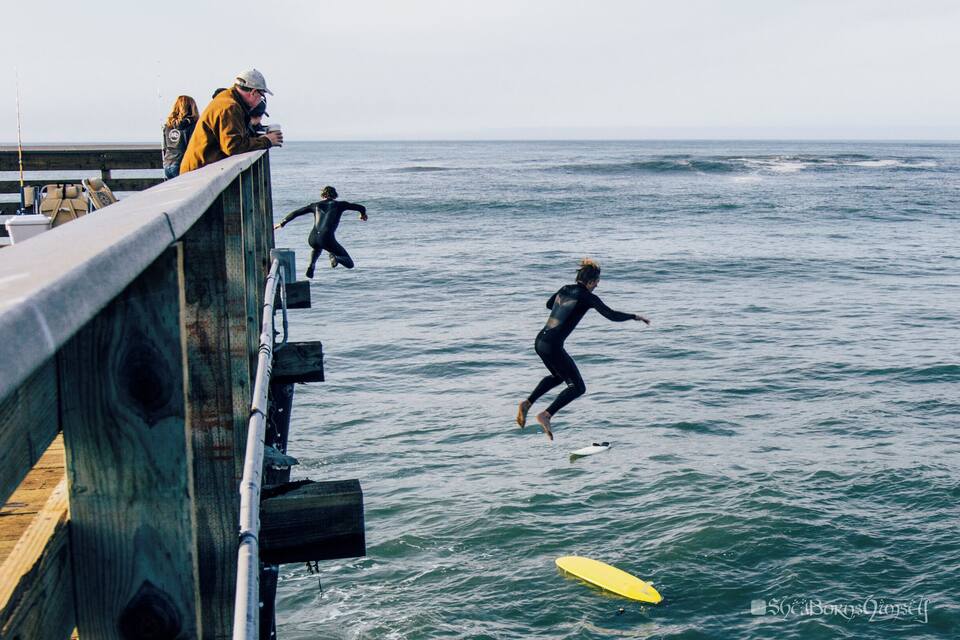 A wooden pier with people surfing in the ocean.