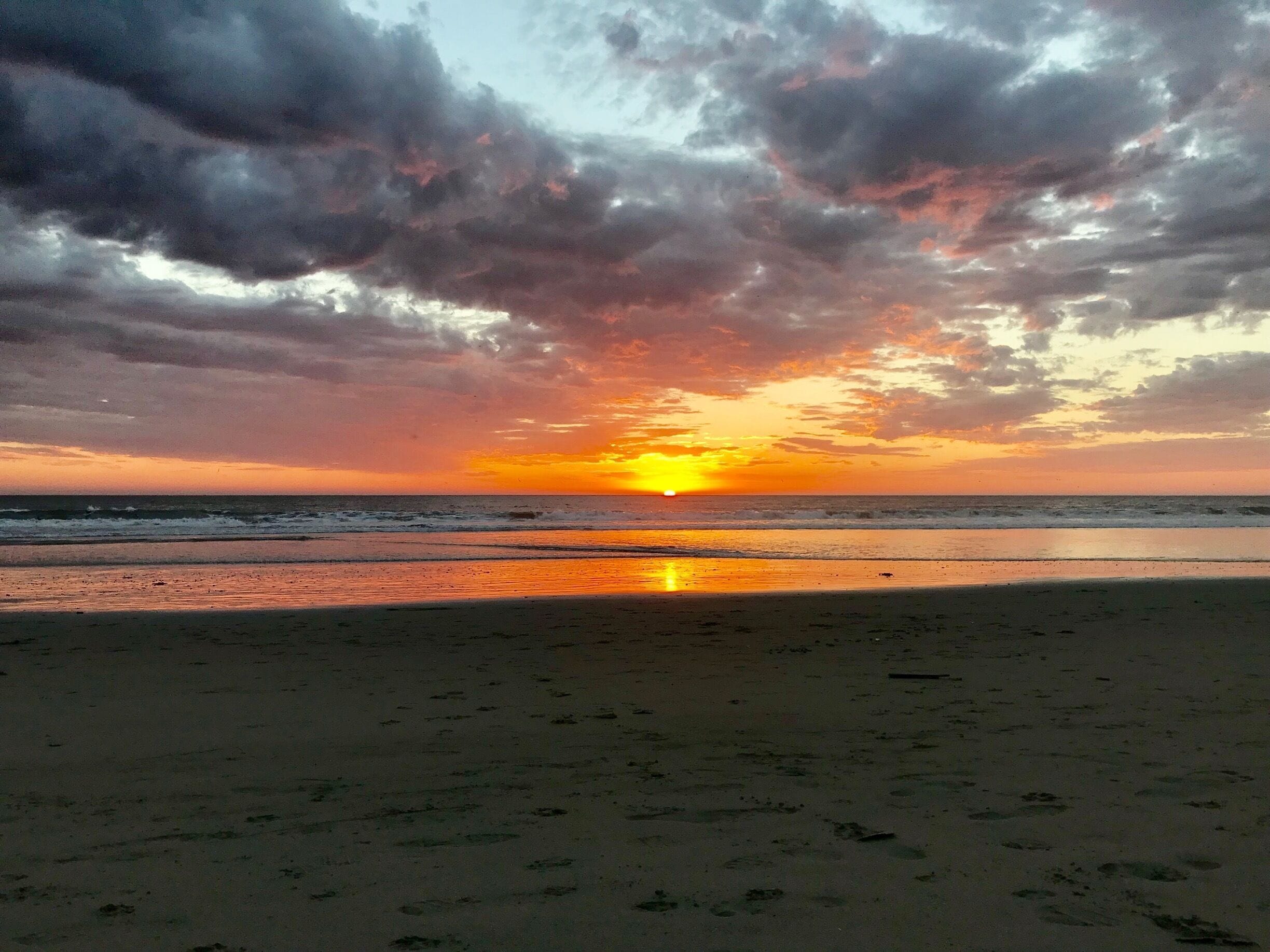 A beach at sunset with a cloudy sky.