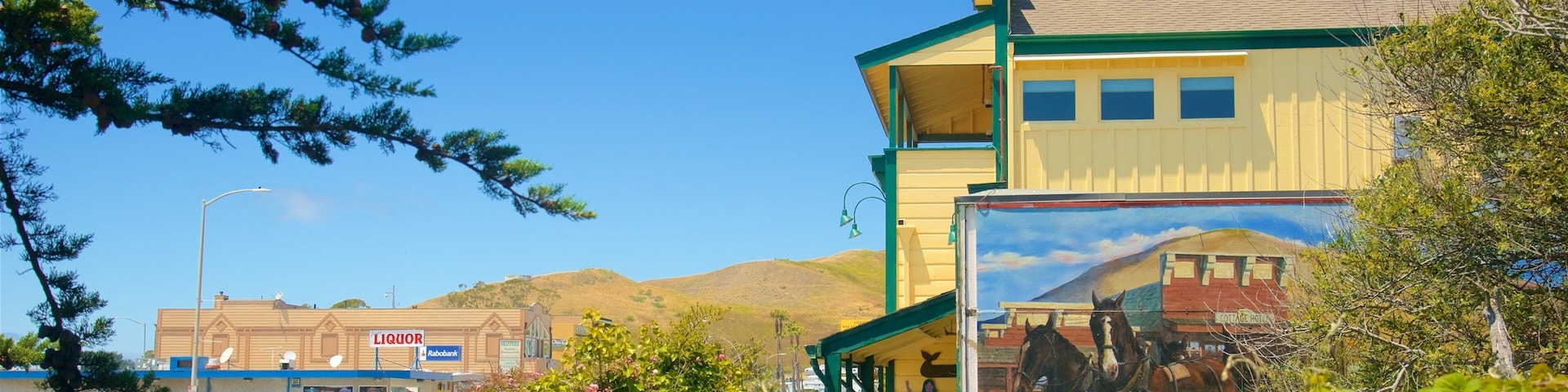 A building with a mural of horses, surrounded by greenery and a clear blue sky.