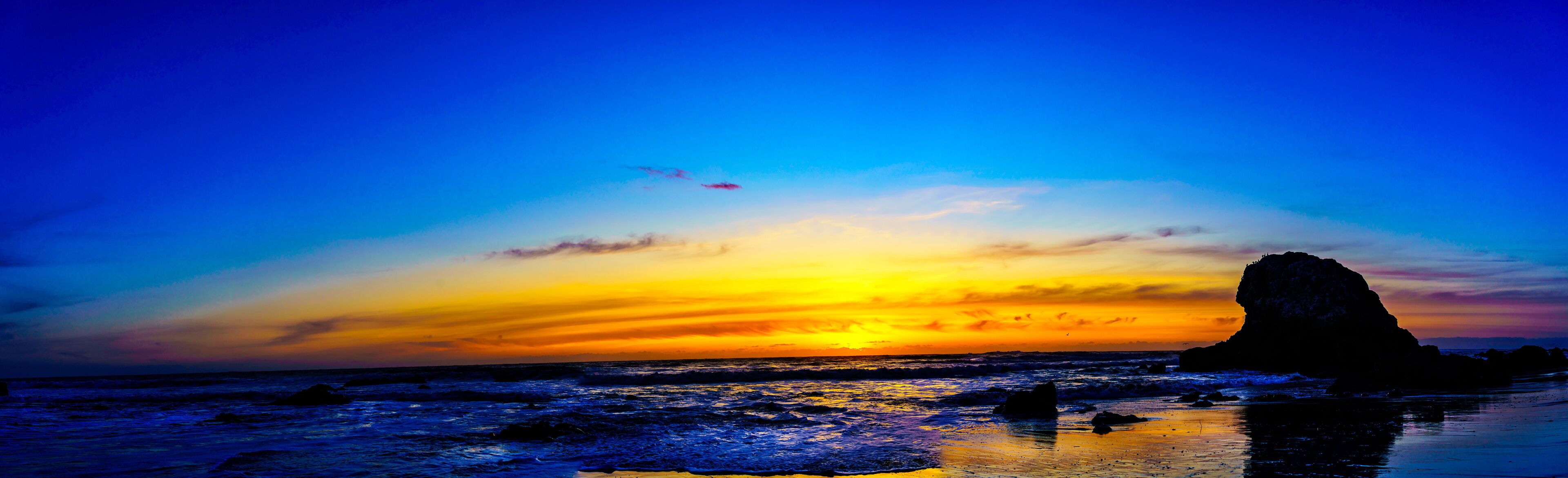 Un atardecer sobre una playa con una formación rocosa destacada.
