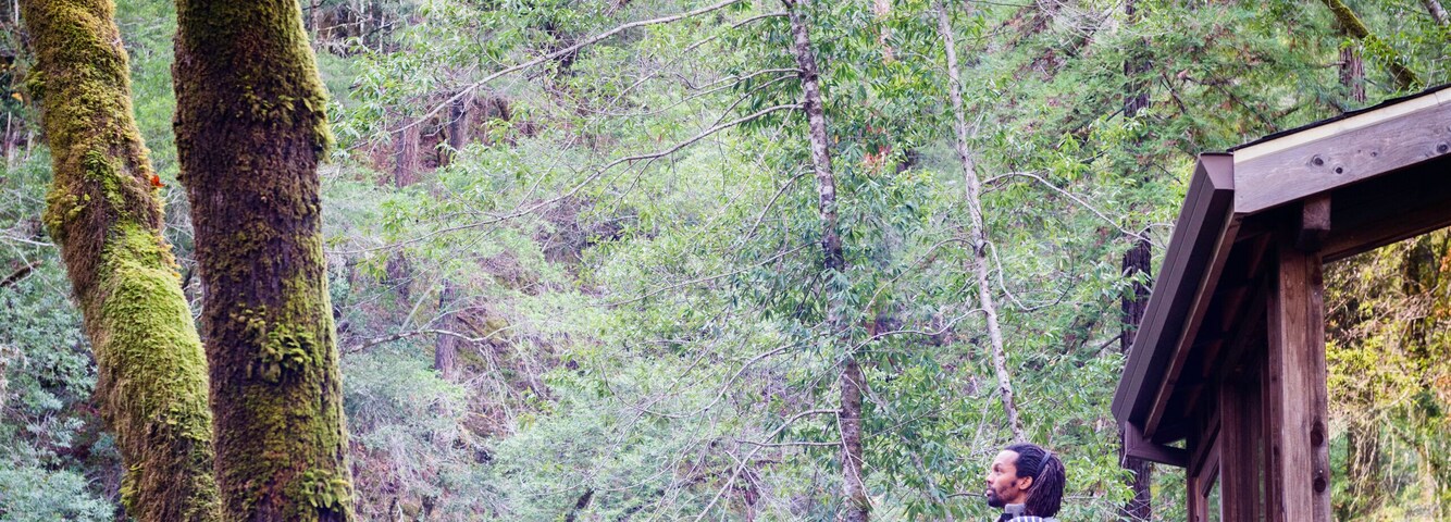 Father with baby son on balcony of stilted wooden house in forest, Cazadero, California, USA