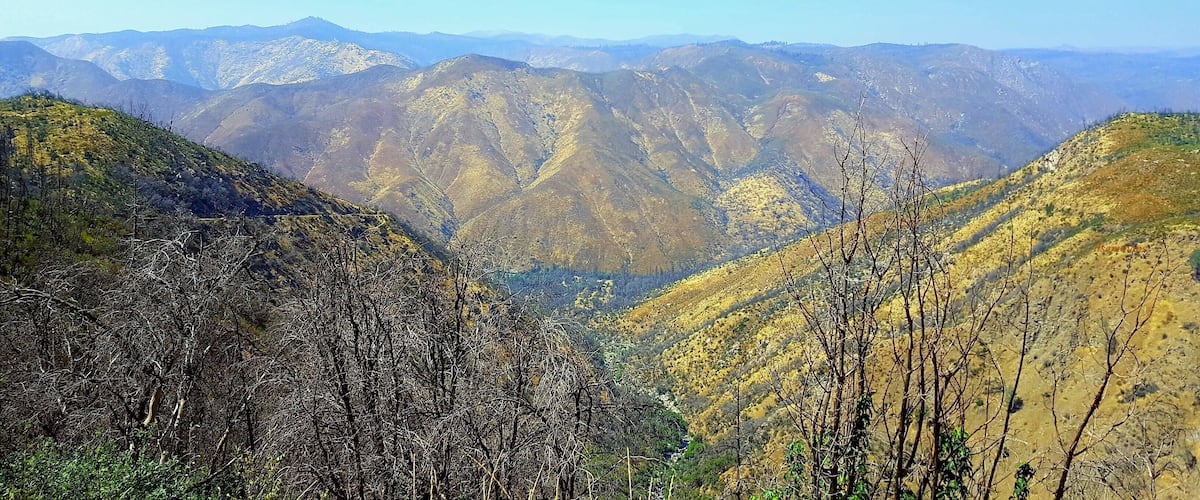 A mountainous landscape with a valley and distant hills under a clear sky.