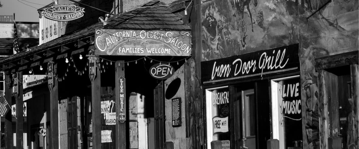 Une photographie en noir et blanc d’un bâtiment historique, sur laquelle on peut voir des enseignes indiquant « Iron Door Saloon » et « California Oldest Saloon ».