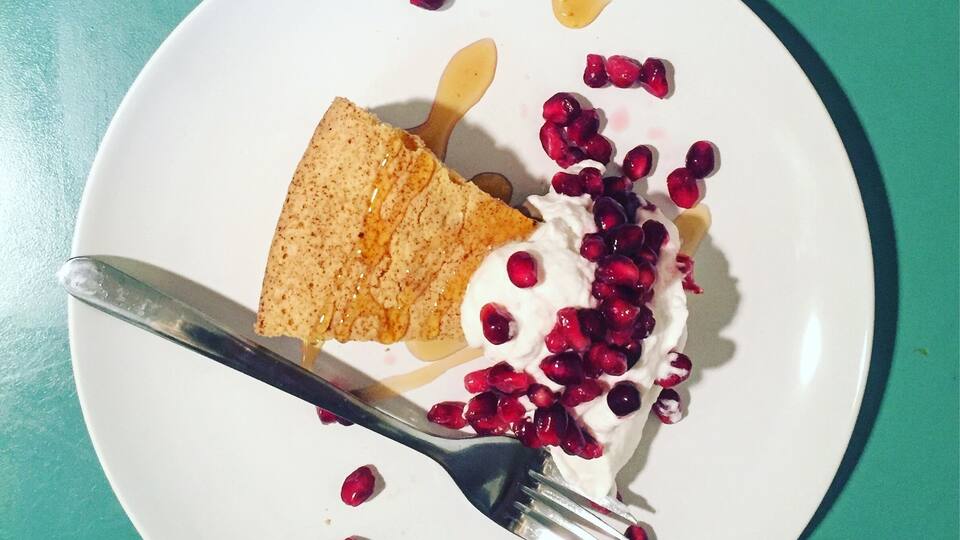 A slice of cake with whipped cream and pomegranate seeds on a white plate.