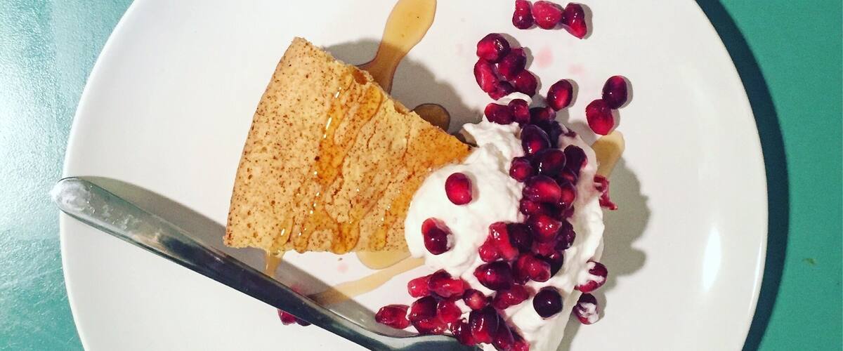 A slice of cake with whipped cream and pomegranate seeds on a white plate.