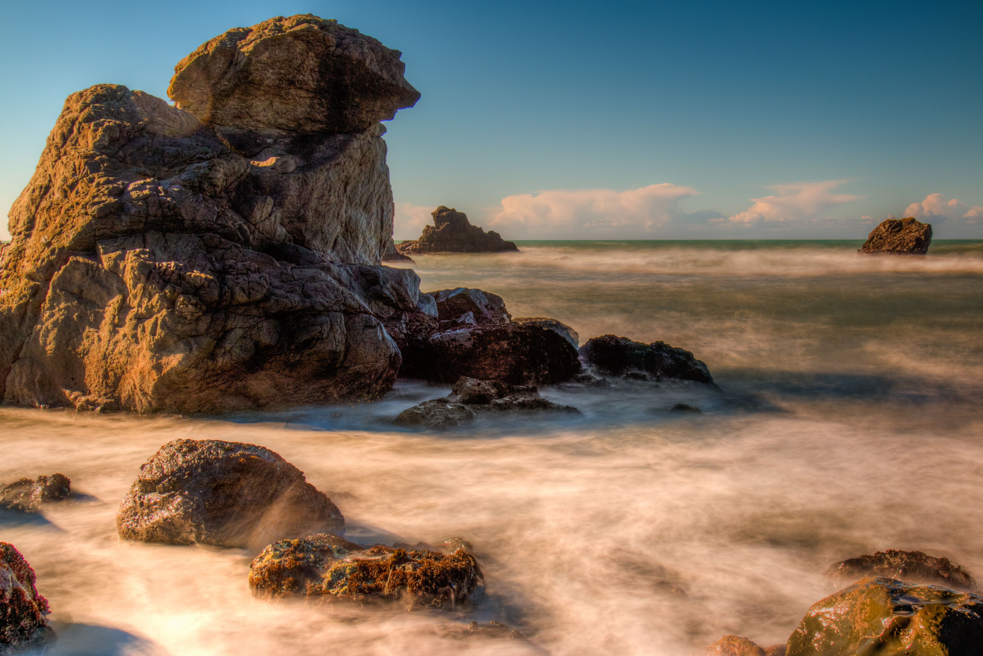 A rocky coastline with large boulders and a calm sea.